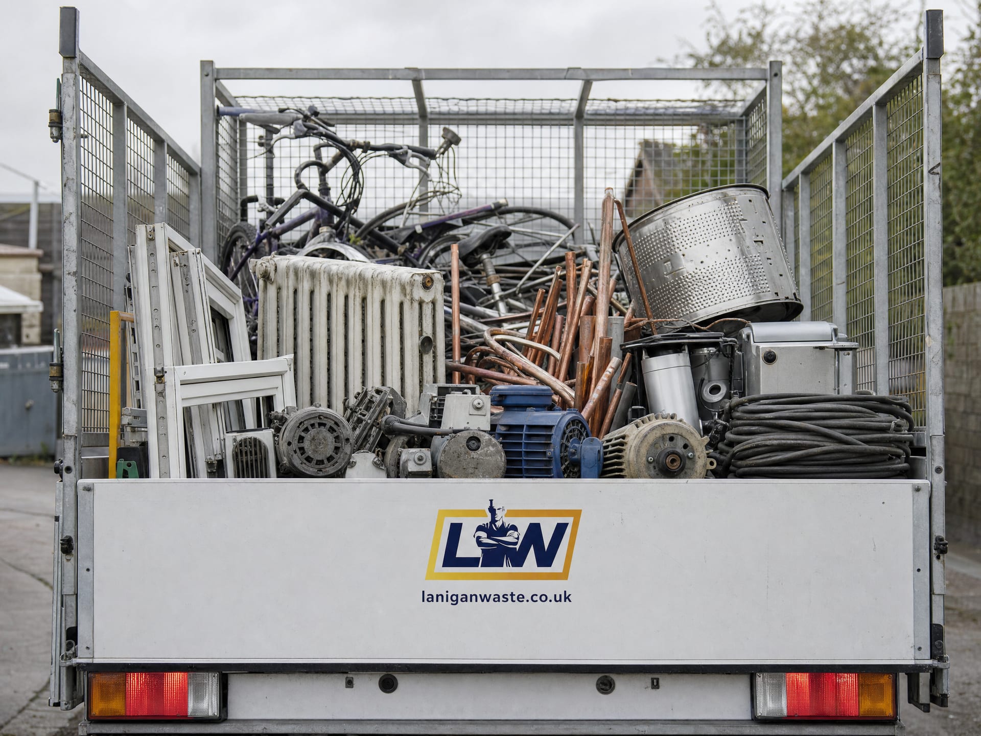 Sorted scrap metal, bikes and copper piping in a branded Lanigan Waste cage trailer